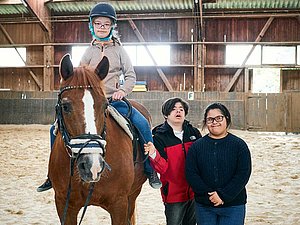 Die Kinder Emma, Teoman und Liya in der Reithalle bei der Reittherapie