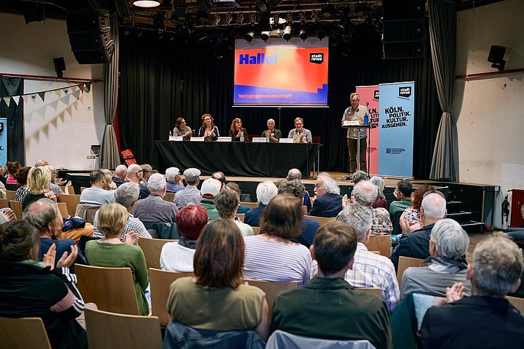 Das erste Treffen der Stadtrevue-Verlagsgenossenschaft im Juni 2026: Auf dem Podium stellt sich der Vorstand den Fragen aus dem gut gefüllten Saal des Büze Ehrenfeld ist gut besucht.