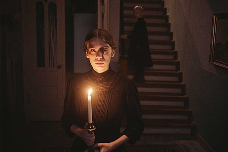 Filmszene aus Mascha Schilinskis Film»In die Sonne schauen«: eine junge Frau steht mit einer brennenden Kerze in einem dunklen Treppenhaus