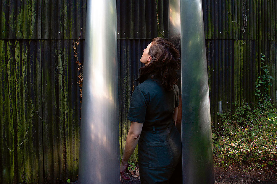 Künstlerin in der eigenen Installation stehend: Olga Holzschuh, songs of conditions, 2024, Schwarze Erde, Aluminium, Kupfer.